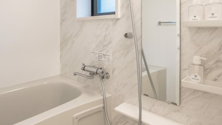 Clean bathroom with a deep white bathtub, shower hardware, and white marbled wall panels, featuring built-in shelving for toiletries.