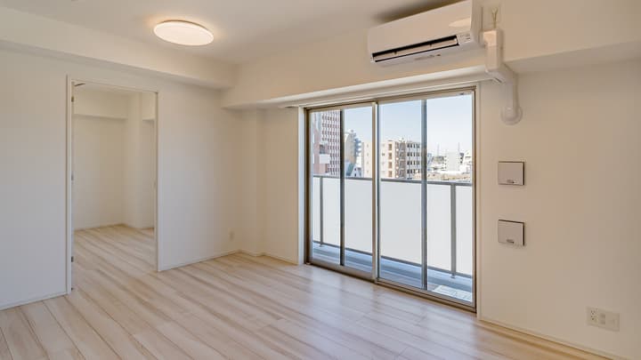 Sunlit bedroom with light wood-style flooring, a wall-mounted air conditioner, a large sliding glass door to a balcony, and an open doorway leading to a walk-in closet or adjacent room.