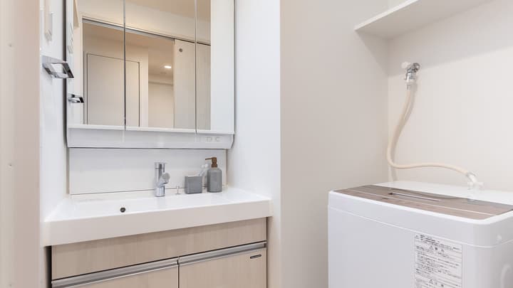 Modern bathroom vanity with a large mirrored cabinet and sink, next to an area containing an in-unit washing machine.