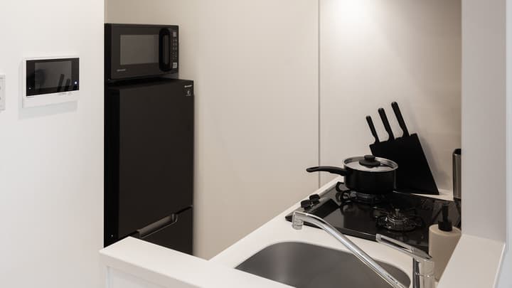 Compact white kitchen area with a small black refrigerator, microwave, sink, and two-burner gas stovetop with a black knife block.