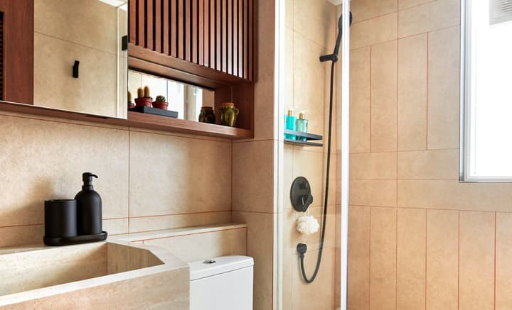 Contemporary bathroom featuring neutral-toned, textured wall tiles, a sleek glass shower enclosure with matte black fixtures, and a vanity area with wooden slatted storage.