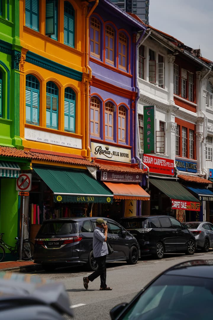 Street view showing the vibrant and colorful facades of historic Kampong Glam shophouses in Singapore, with shops like Rania Silk House below.