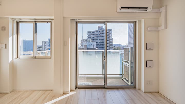 Close-up view of the living room, showing the wall-mounted air conditioner, a smaller window, and the large sliding glass door leading to a balcony with a city view.