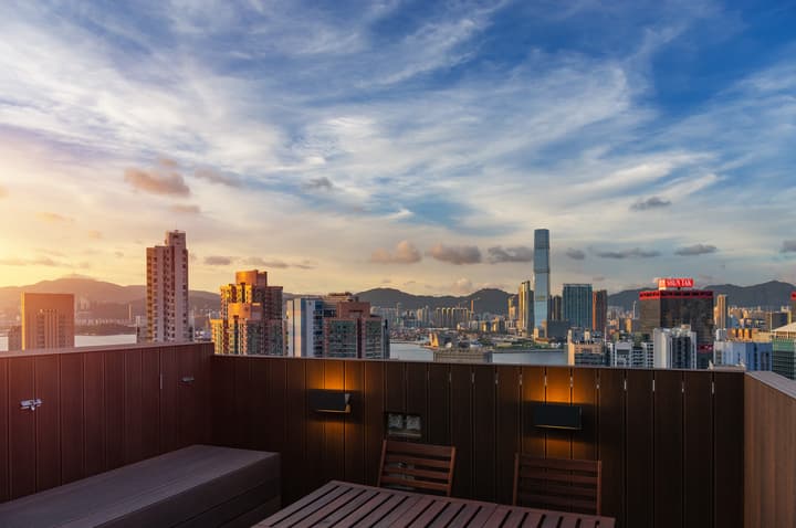 Stunning sunset view of the Hong Kong skyline and mountains from a modern rooftop terrace with wooden decking and outdoor seating.