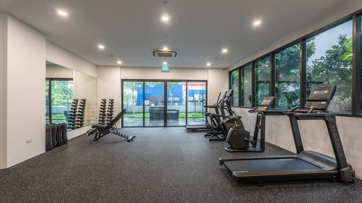 Interior of the apartment building's fitness center featuring a treadmill, elliptical machines, free weights rack, and floor-to-ceiling windows.