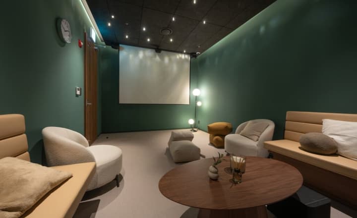 Cozy private screening room with a large projector screen, dark green walls, modern lounge furniture, and a round wooden coffee table.
