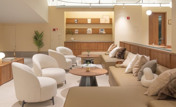 Comfortable resident lounge area furnished with curved, cream-colored armchairs, long sofas, and round wood coffee tables.