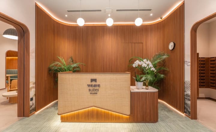 Modern lobby and reception area with a curved, textured reception desk, vertical wood slat paneling, illuminated archways, and minimal overhead lighting.