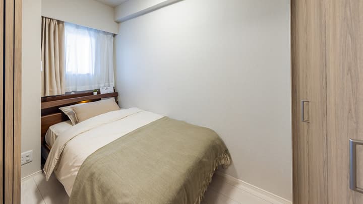 Cozy bedroom with light wood-style flooring, a single bed with a tan blanket, a window with curtains, and a light wood-effect wardrobe in Monzennakacho.