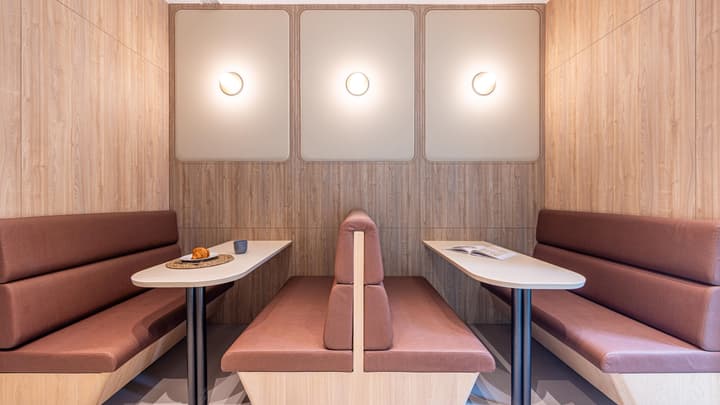 A close-up of a cozy, private communal seating nook featuring opposing brown upholstered booths, small tables, and wood-paneled walls with decorative lighting.