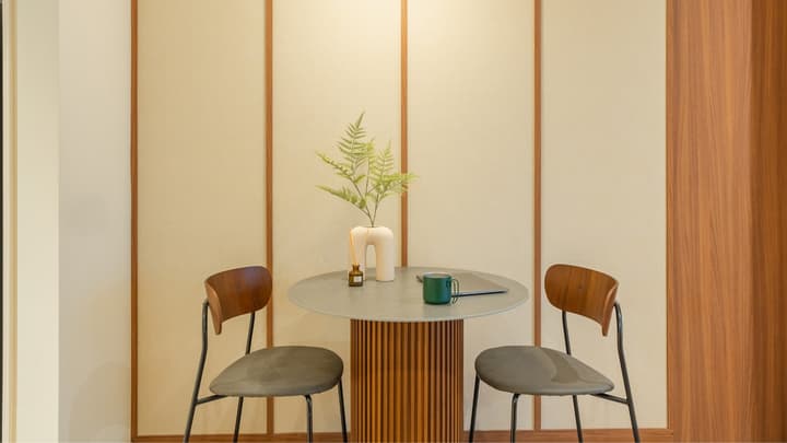 Close-up of a small, two-person dining area with a round grey table featuring a fluted wooden base, and two mid-century style chairs.