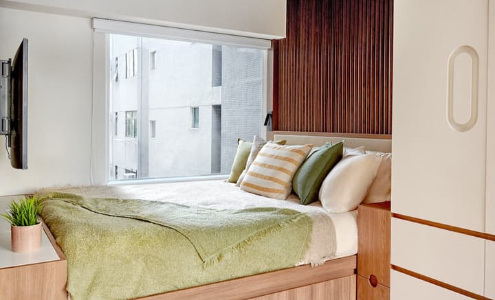 Cozy, modern bedroom featuring a light wood platform bed with green and striped pillows, a warm wooden slatted accent wall, and a large horizontal window.