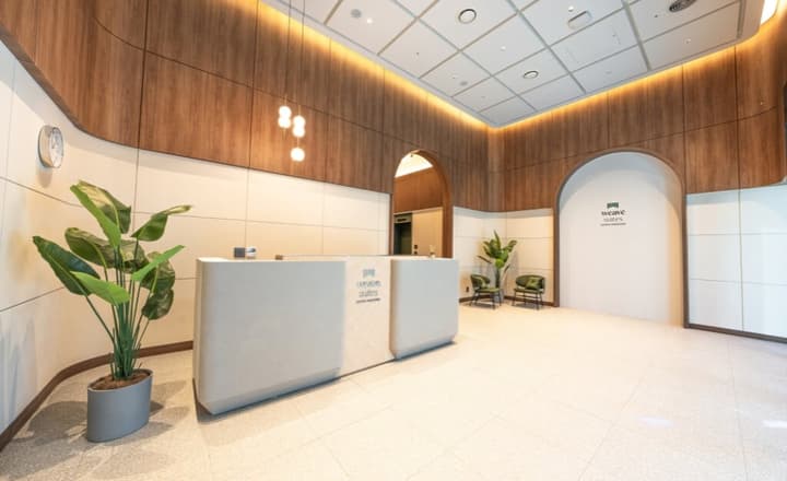 Bright, modern building lobby featuring a curved white reception desk, wood paneling, arched doorways, and a large potted plant.
