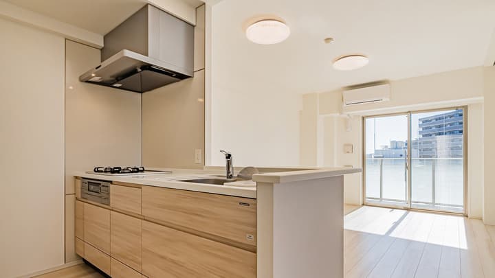 Modern kitchen with a gas cooktop, under-counter oven, stainless steel sink, light wood lower cabinets, white counters, and a large stainless steel range hood.