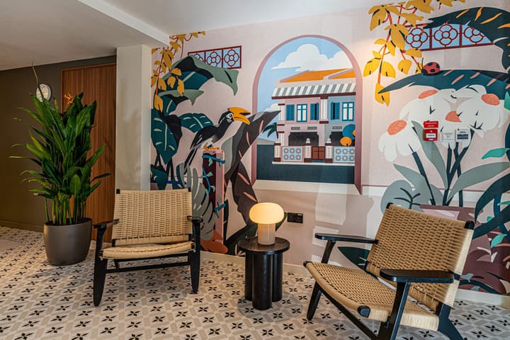 Vibrant lobby seating area with a colorful, tropical-themed mural, patterned floor tiles, and two woven rattan armchairs.