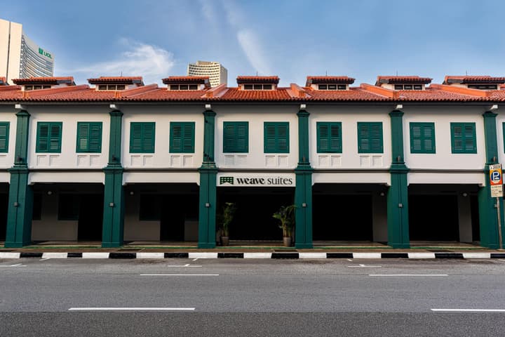 Exterior view of the Weave Suites entrance in a traditional Singaporean shophouse building with white walls and green columns and shutters.