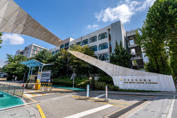 The main entrance gate of Seoul National University of Education, featuring a modern, angular stone sign with Korean and English text, surrounded by trees on a sunny day.