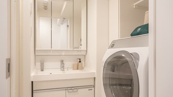 Bathroom vanity area with a sink and mirrored medicine cabinet, showing a reflection of the room and a front-loading washer-dryer combination unit to the right.