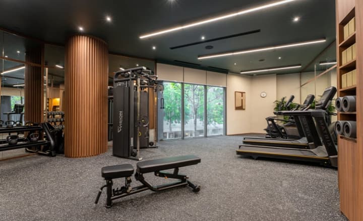 Modern gym and fitness center with a dark rubber floor, exercise machines, treadmills by a large window, and dark green accent walls.