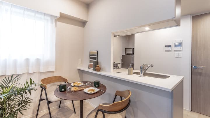 Cozy dining nook with a dark round table, two modern wooden chairs, and a countertop pass-through window looking into the main kitchen area.