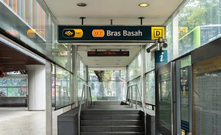 Bras Basah MRT station entrance with steps leading up, showing the overhead CC2 station signage and a glass walkway.