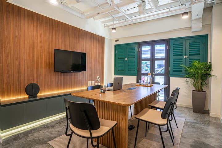 Communal meeting room featuring a large wood table, comfortable chairs, a wall-mounted TV, and vibrant green window shutters.