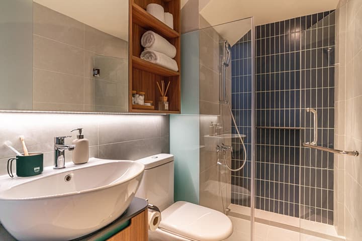 Modern bathroom in the Loft Suite featuring a white oval vessel sink, a walk-in shower with striking navy blue vertical subway tiles, and built-in wooden shelving.