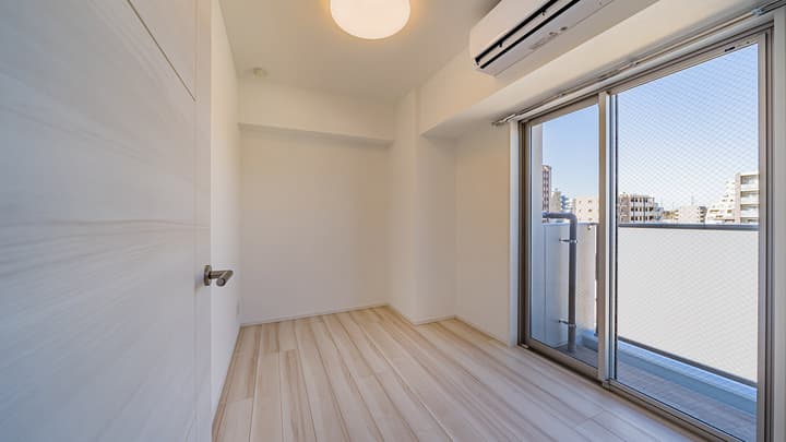Small, empty room featuring light wood-style flooring, a white closet door on the left, an air conditioner, and a large sliding glass door opening to a private balcony.