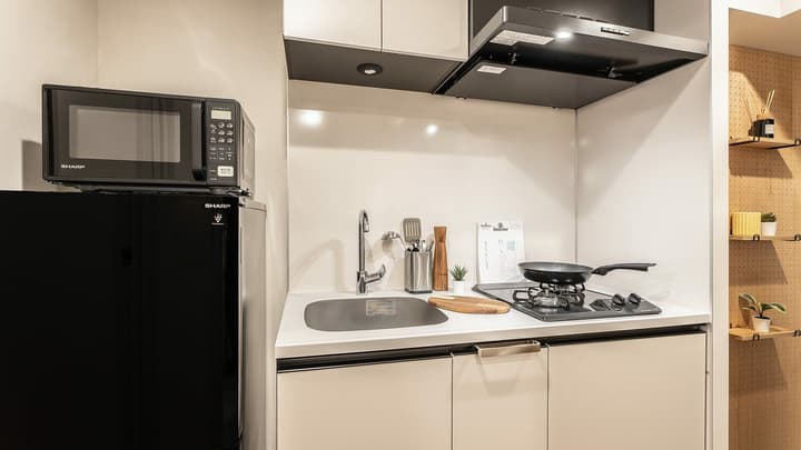Room Type GalleryaCompact kitchen setup in a 1K unit, featuring a black microwave and mini-fridge, sink, two-burner gas cooktop, and beige cabinets.