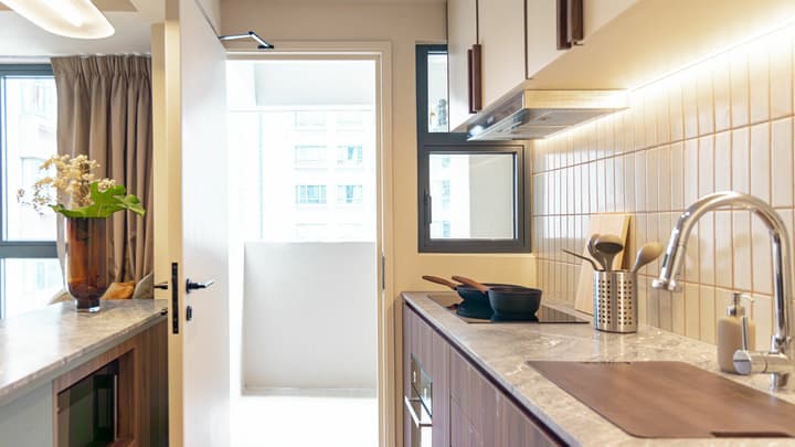 Close-up of a modern open kitchen with wood base cabinets, a marble countertop, an induction cooktop, and a doorway leading out to a small balcony area.