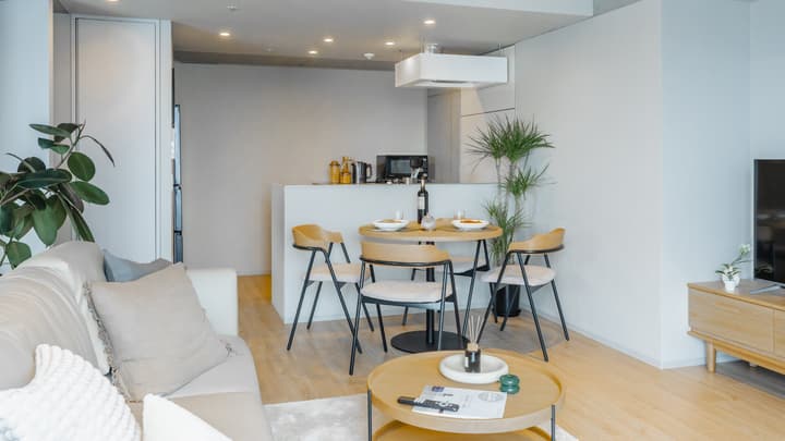 Open-concept view of the living and dining area, featuring a round dining table with four chairs, set against a counter that separates it from the compact kitchen.