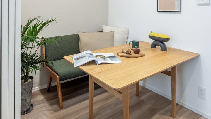 Bright dining nook featuring a square light wood table, a fixed green upholstered bench seat, and a decorative potted plant.