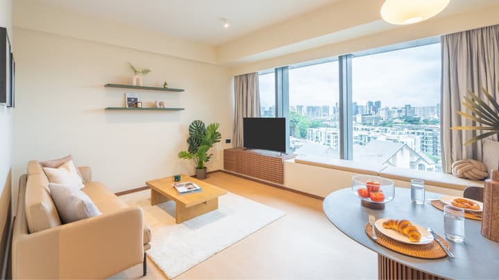 Bright open-concept apartment living and dining area with light wood floors and a large, wide window offering a city view.