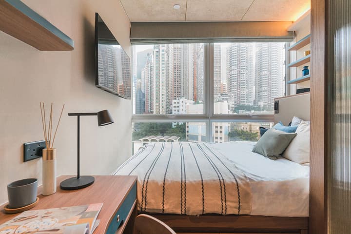Modern Premium Suite bedroom at Weave Suites – Central West, featuring a queen bed with black and white stripes, a built-in desk, wall-mounted TV, and large windows with a city skyline view.