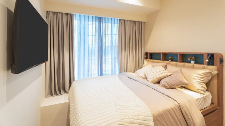 Primary bedroom with a queen bed, upholstered headboard with storage, and a large wall-mounted TV facing the bed and the window.