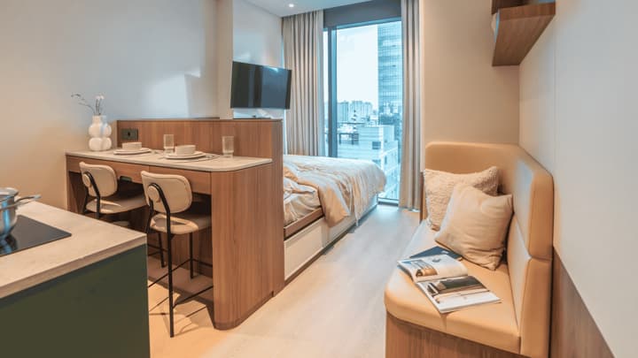 Full view of the Premium Suite Double featuring a double bed, a dining/desk counter, and a built-in tan leather bench/sofa on the right, providing a dedicated lounge area by the window.