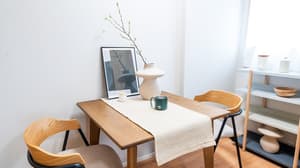 Close-up of a wooden dining table set with two modern chairs, featuring a white vase with decorative branches and a framed picture on the table in Monzennakacho.