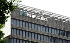 Close-up of the exterior of the Weave Suites building showing the logo and signage against the modern facade with glass windows and horizontal slat paneling.