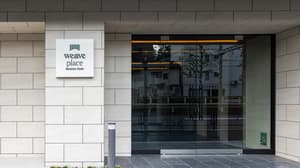 The modern, tiled main entrance of the 'Weave Place Waseda Park' residential building, featuring a sign with the logo and a clear glass facade.