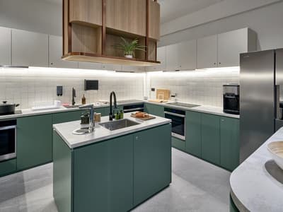 Spacious, contemporary shared kitchen with matte green cabinets, white square backsplash tiles, a center island with a sink, and stainless steel appliances.