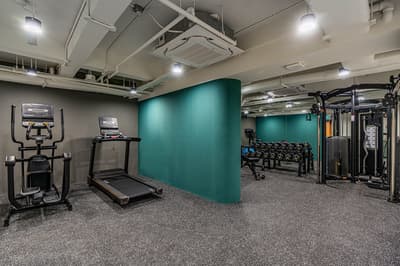 Well-equipped apartment gym with a treadmill, elliptical machine, rack of free weights, and a teal-colored curved accent wall.
