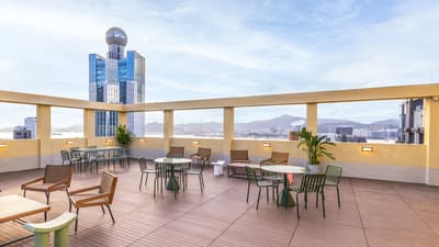 Outdoor rooftop terrace with wood decking and various seating groups, offering a panoramic view of the city skyline, mountains, and a distant harbour.