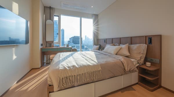 The separate bedroom of the luxe suite, featuring a queen bed with under-bed storage, a stylish wood headboard with integrated lighting, and a window-facing dressing table/desk.