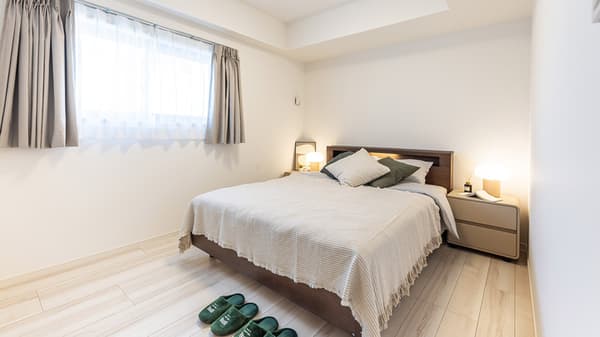 Spacious bedroom with a double bed, light wood frame, matching modern nightstands with glowing lamps, and a large bright window with gray curtains.