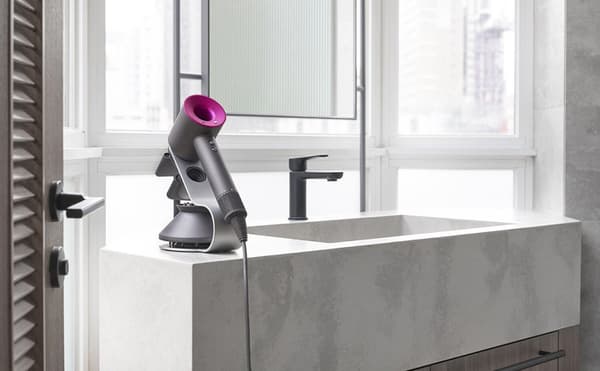 A modern bathroom counter with a large, square concrete sink, black faucet, and a purple Dyson hair dryer on a stand next to a window with a city view.