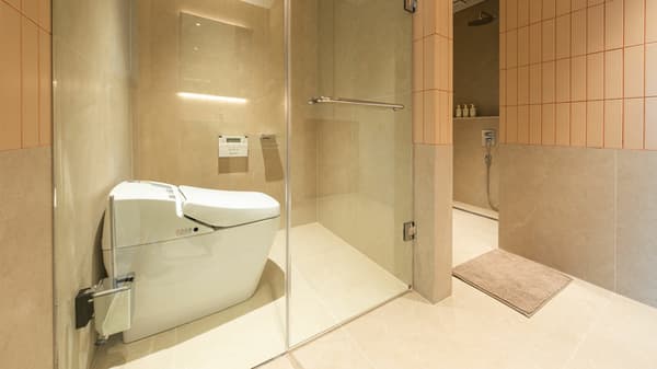 Luxurious bathroom with a glass-enclosed walk-in shower area and a modern smart toilet, featuring large-format beige tiles on the floor and walls.
