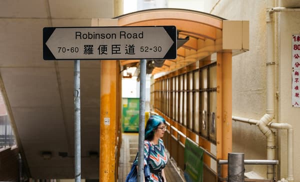 Street-level view of a 'Robinson Road' sign in English and Chinese, with a person walking on a covered, elevated pedestrian walkway in the background.