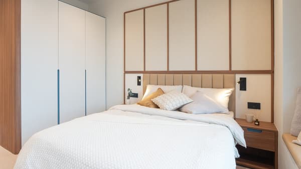 Close-up of the queen bed with bright white bedding, upholstered headboard, wooden side table, and a white, floor-to-ceiling built-in wardrobe.