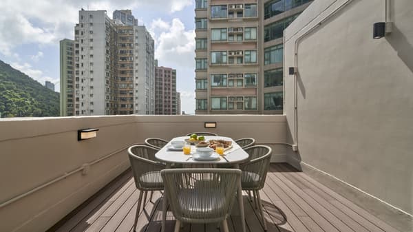 Modern rooftop deck with composite wood flooring, featuring an oval dining table and woven chairs, set against a backdrop of tall residential city buildings.