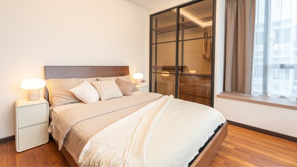 Bedroom with a queen-sized bed, neutral-toned bedding, two glowing bedside lamps, and a glass-paneled closet door leading to a walk-in wardrobe.